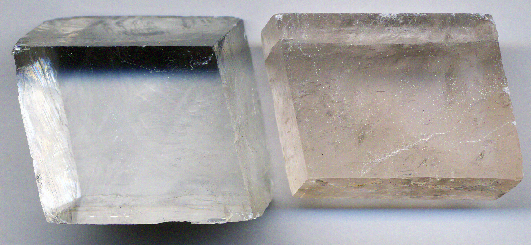 Several clear calcite fragments that have broken into identical rhombohedron shapes, showing perfect cleavage along three directions