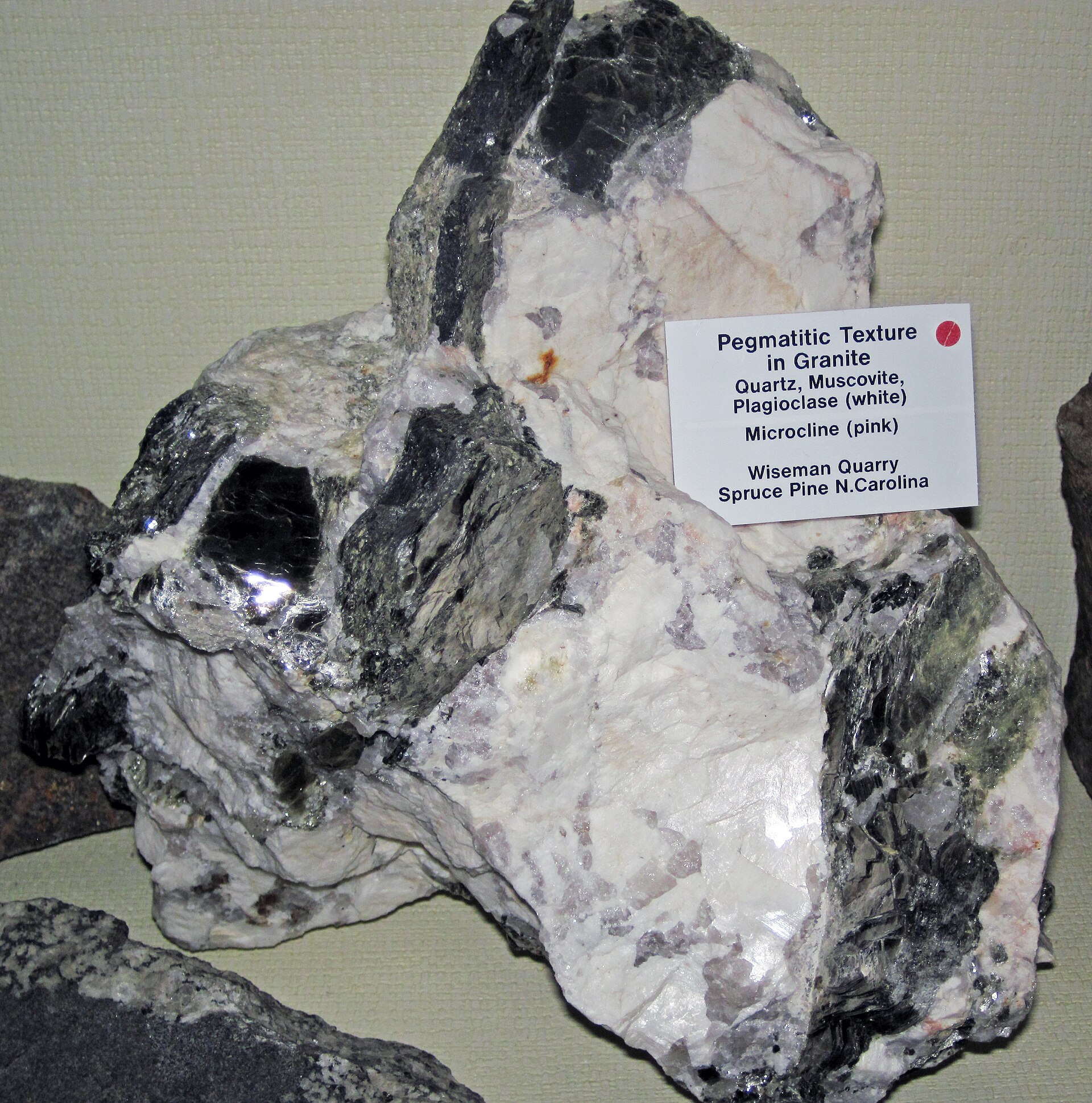 Close-up of pegmatitic granite showing grey glassy quartz, pink and white feldspar, and dark flaky mica grains locked together in one rock