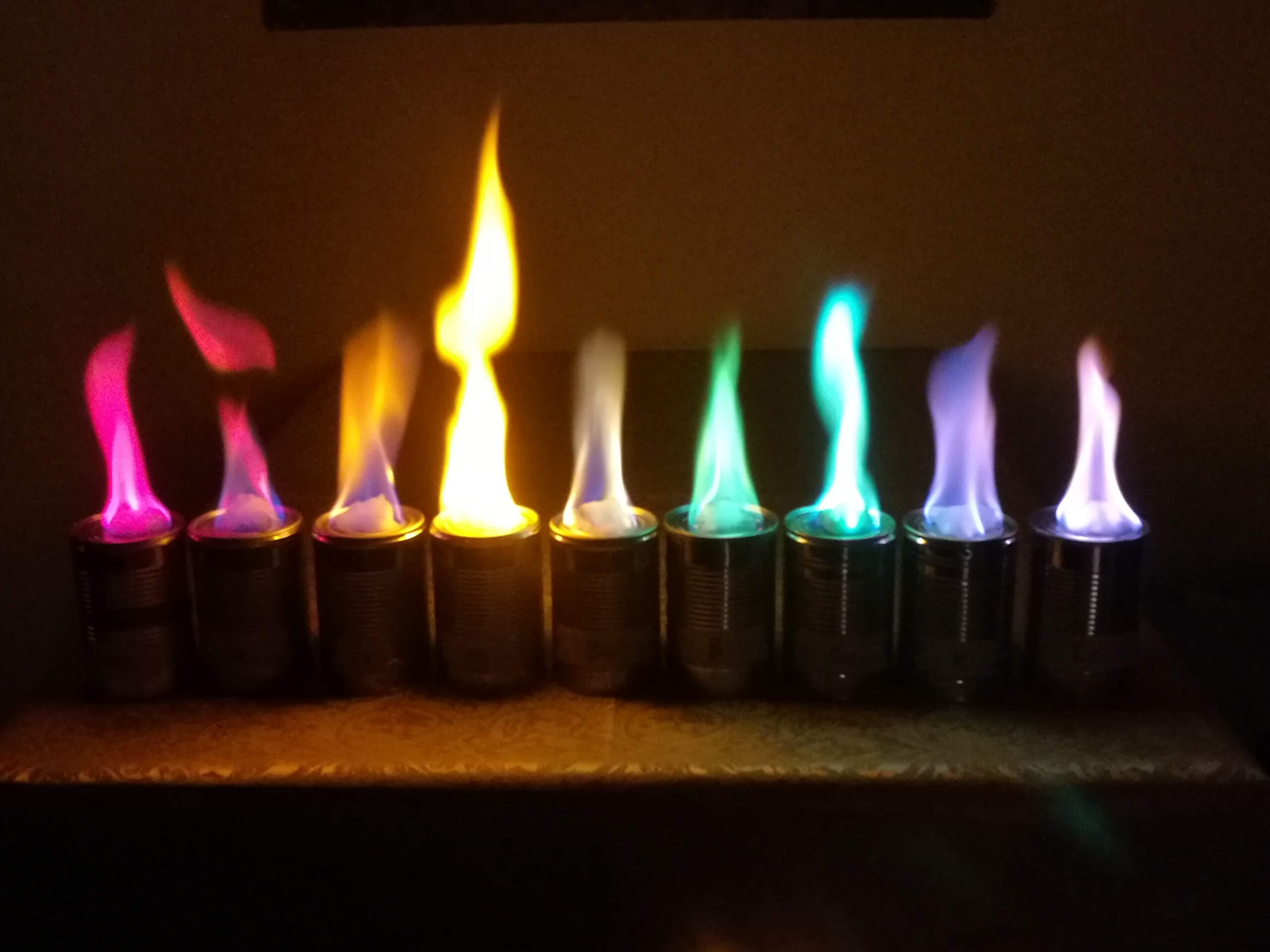 A row of flames burning different colours from methanol solutions of metal salts, illustrating the flame test