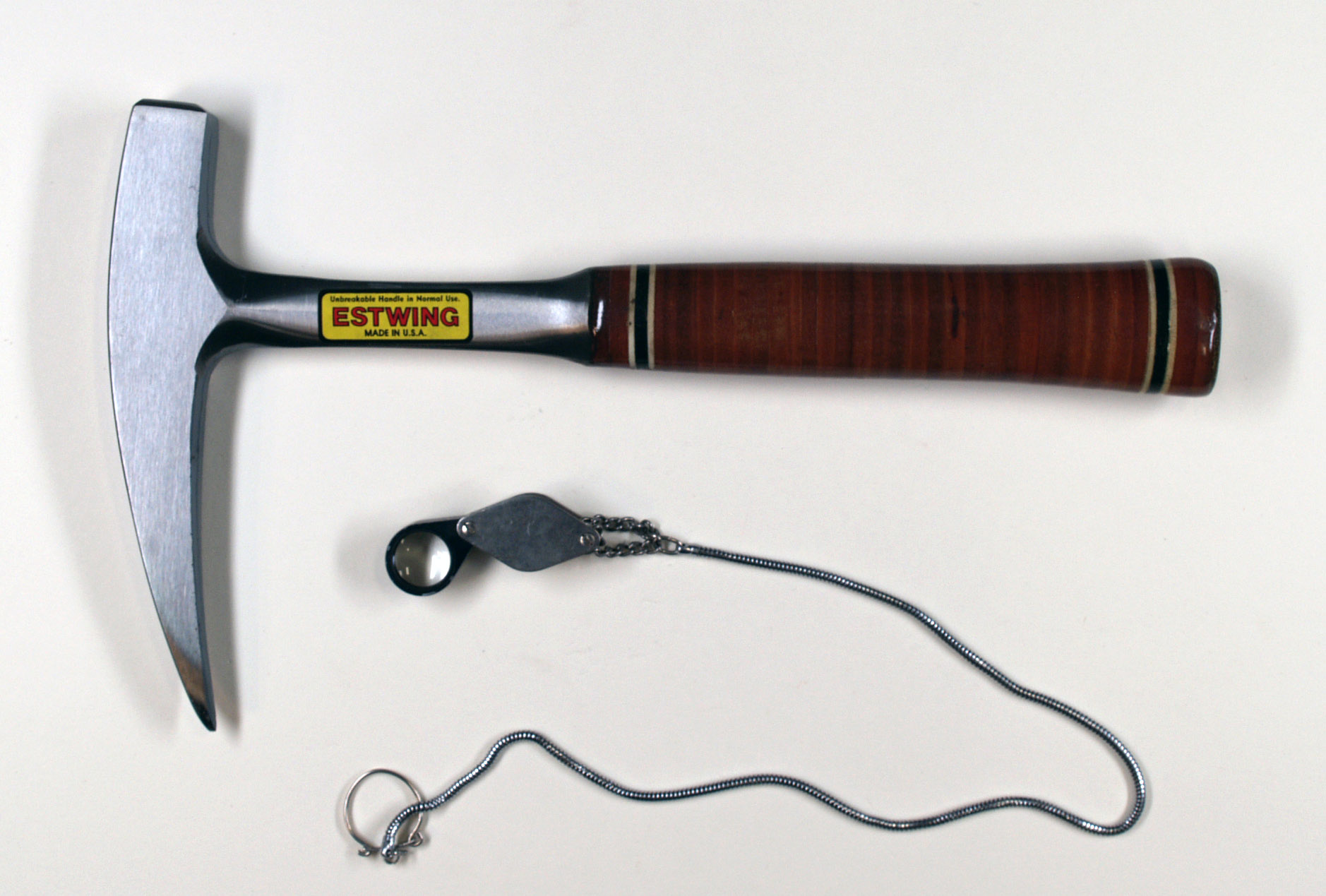 A geologist's hand lens (loupe) alongside a rock hammer and compass